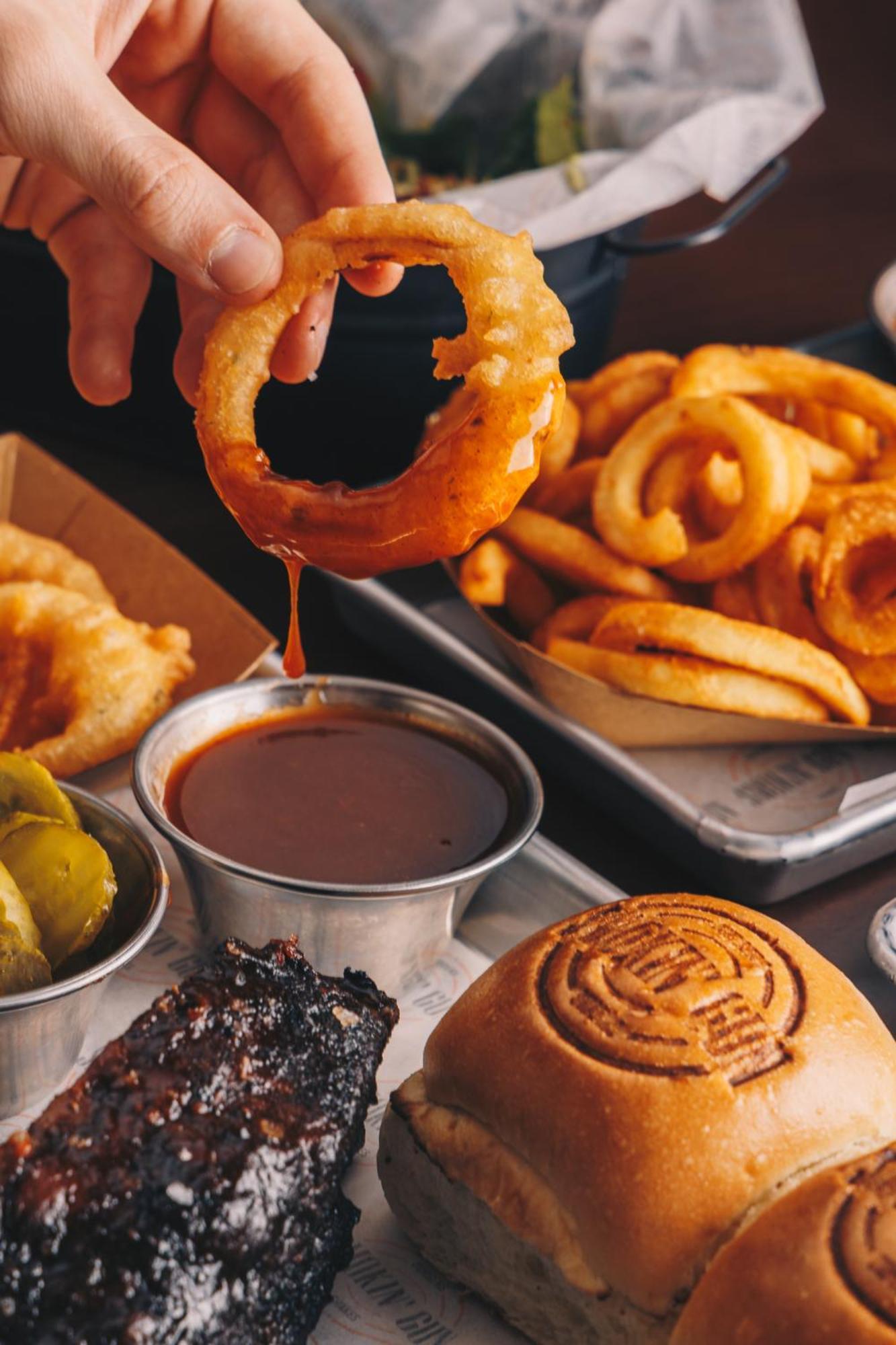 Ja The Resort - Ja Lake View Hotel, Dubai Luaran gambar A hand dipping an onion ring into a bowl of barbecue sauce